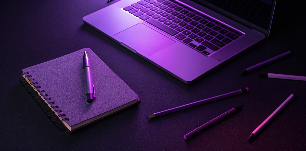 A laptop, pen, and notebook on a table with purple lighting, ideal for organizing hotel bookings